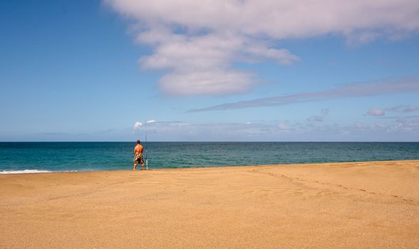 Rear view of fisherman on a wide sandy beach