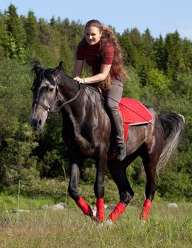 Girl astride a horse galloping on a background of green wood