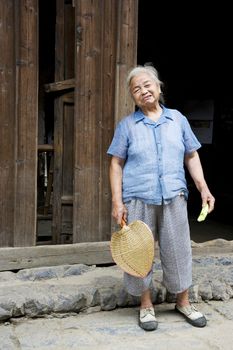 Image of an elderly Chinese lady with fan and cucumber in hand at Daxu Ancient Town, Guilin, China.