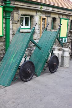 A pair of vintage wooden constructed baggage trollys on the platform of Swanage Railway in Dorset, UK. Set against a station building with two milk churns.