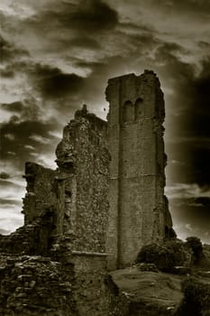 A mono image of Corfe Castle in Dorset with a dramatic cloud background and rolling fog at dusk.