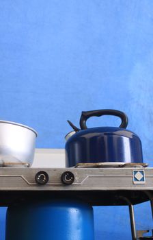 A blue kettle on top of a camping gas stove, set against a bue canvas tent background.