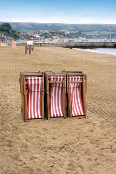 A set of stacked red and white stripped deck chairs on the beach at Swanage in Dorset, UK.