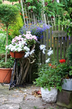 A garden gate marked 'private' surrounded by potted plants and flowers on a stone path.
