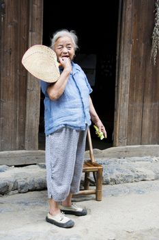 Image of an elderly Chinese lady with fan and cucumber in hand at Daxu Ancient Town, Guilin, China.