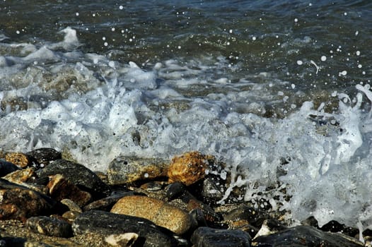 Sea foam splashing against pebbles