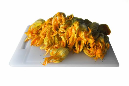 Zucchini flowers on chopping board against white background