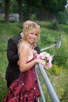 Bride and groom leaning over a meadow fence