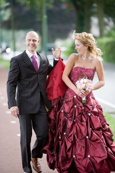 Pretty wedding couple walking while the man is holding her dress