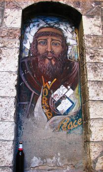A fresco on the streets of a hippie in a niche in Assisi, Italy with an accompanying beer bottle.