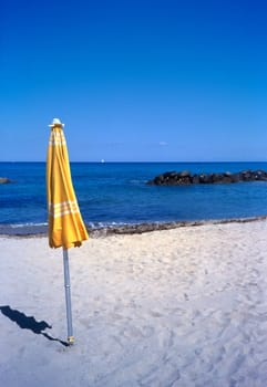 Yellow closed umbrella on a beach