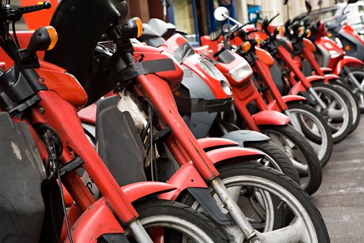 Many red motorcycles stand in a row
