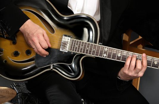 electric guitar close-up with fingers playing it
