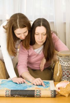 Mother and the daughter consider a world card in apartment in an environment of subjects
