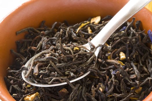 Dry green tea with slices of orange-peels and a bergamot in a clay bowl with spoon close up
