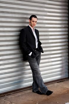 Handsome casual business man standing in front of and leaning against silver metal garage door with hands in pocket