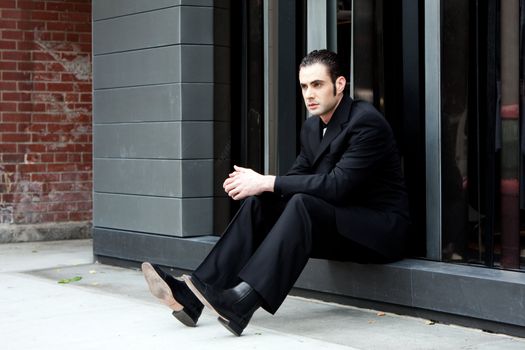 Handsome Caucasian business man in black suit sitting on street in front of a modern building