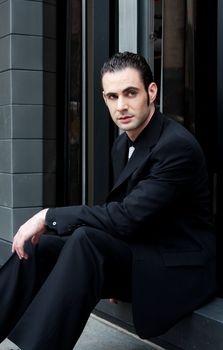 Handsome Caucasian business man in black suit sitting on street in front of a modern building