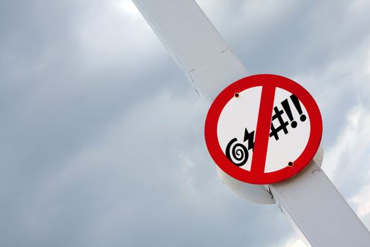 White round traffic street sign with red border that forbids cursing and bad language on a pole with a gray cloud background.