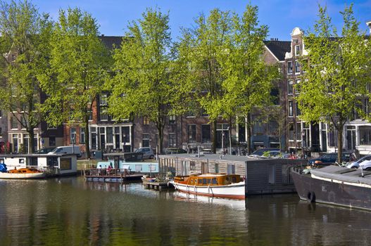 Classic view of Amsterdam. Embankment with barge. Green trees against the background of Dutch houses.