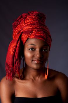 Beautiful African-American woman wearing a traditional tribal red orange head scarf and orange earrings, isolated.