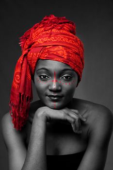 Beautiful traditional African-American woman wearing a authentic tribal red orange head scarf and red dotted makeup, supporting her chin with hand, isolated.