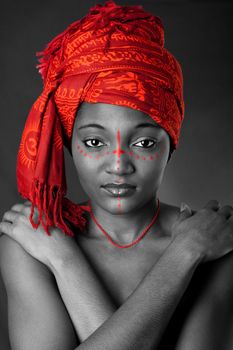 Beautiful traditional African-American woman wearing a authentic tribal red orange head scarf and red dotted makeup, heaving arms crossed on chest, isolated.
