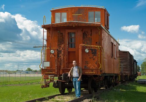 A train caboose shot on a partly cloudy day along with a young man to show the size of it