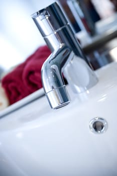tap of a clean washbasin with red towels on the background