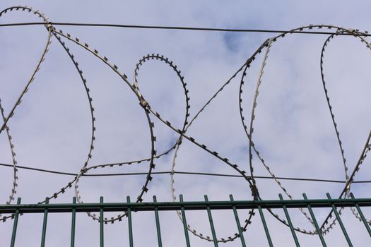 High-security fence with razor wire crown before partly clouded blue sky.