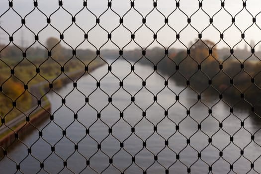 Netting of linked steel cable in front of distant (and blurred) river landscape.