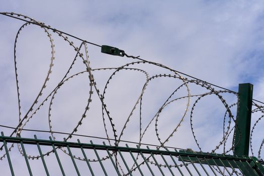 High-security fence with razor wire crown before partly clouded blue sky.