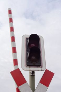 Signal light and open red-white barrier bar at railroad crossing.