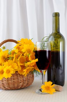 A glass of rose wine with an open bottle and yellow flowers in a basket