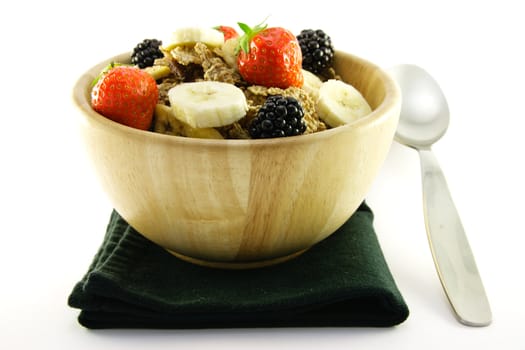 Crunchy delicious looking bran flakes and juicy fruit in a wooden bowl with a spoon and a black napkin on a white background