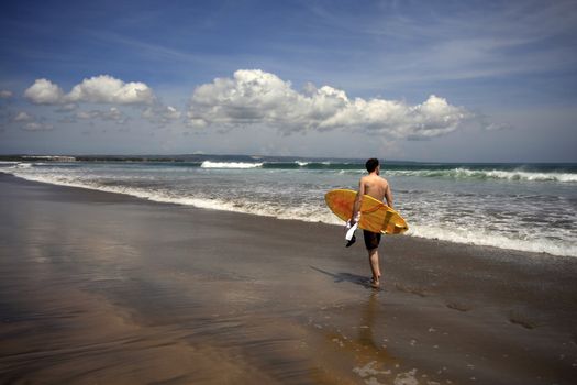 Man-surfer with board on a coastline. Bali. Indonesia