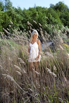 girl in white dress are standing in dry grass at summer daylight