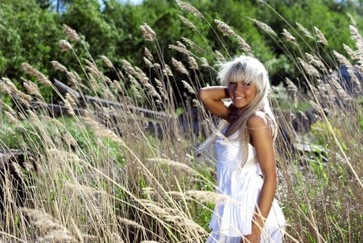 girl in white dress are standing in dry grass at summer daylight