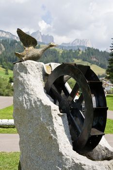 fountain with water moved  wheel and duck sculpture in Soraga, val di Fassa, Italy. On background dolomites mountains