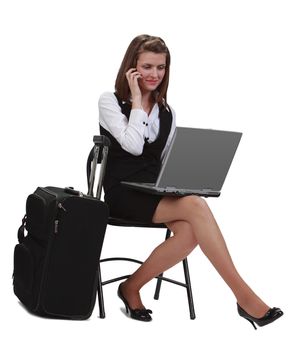 Young traveler businesswoman working on a laptop while is calling by phone next to her suitcase.