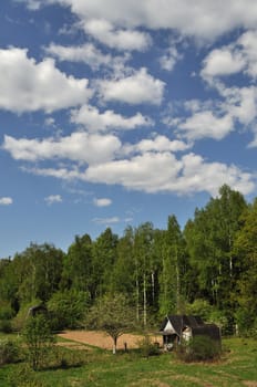 Landscape with old country wooden shacks, spring forest and cloudy sky