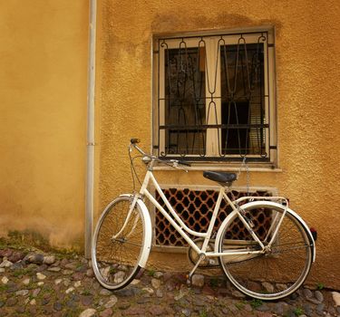 Old bicycle standing against a wall under a window.