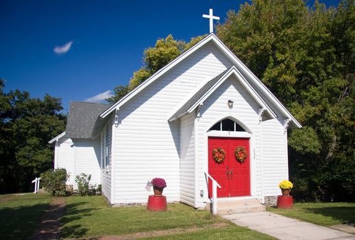 Bright white chapel with red doors decorated with fall flowers