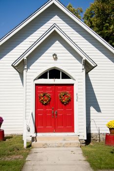 View of bright red church doors decorated with fall wreaths