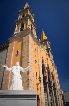 White statue of Jesus in front of the orange cathedral church in Mazatlan