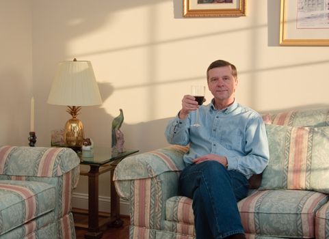 Middle-aged man relaxes on sofa in modern living room drinking a glass of red wine