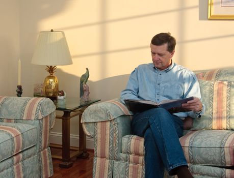 Middle-aged man relaxes on sofa in modern living room reading a book