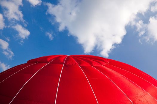 Top of bright red hot air balloon against a blue sky with clouds
