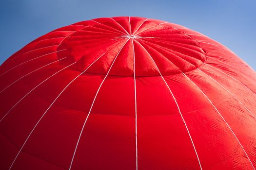 Red canopy of hot air balloon being inflated against a bright blue sky