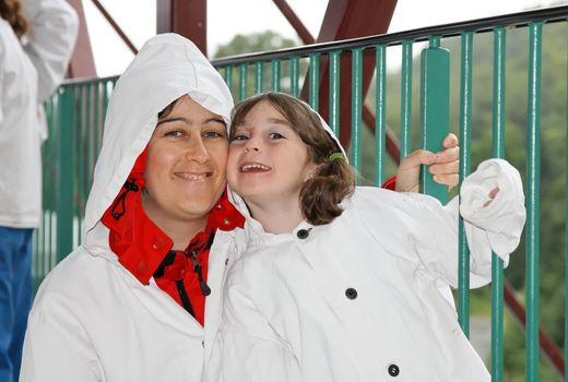 Loving mother and cute preschool daughter in white hooded cloaks cuddling on a bridge 